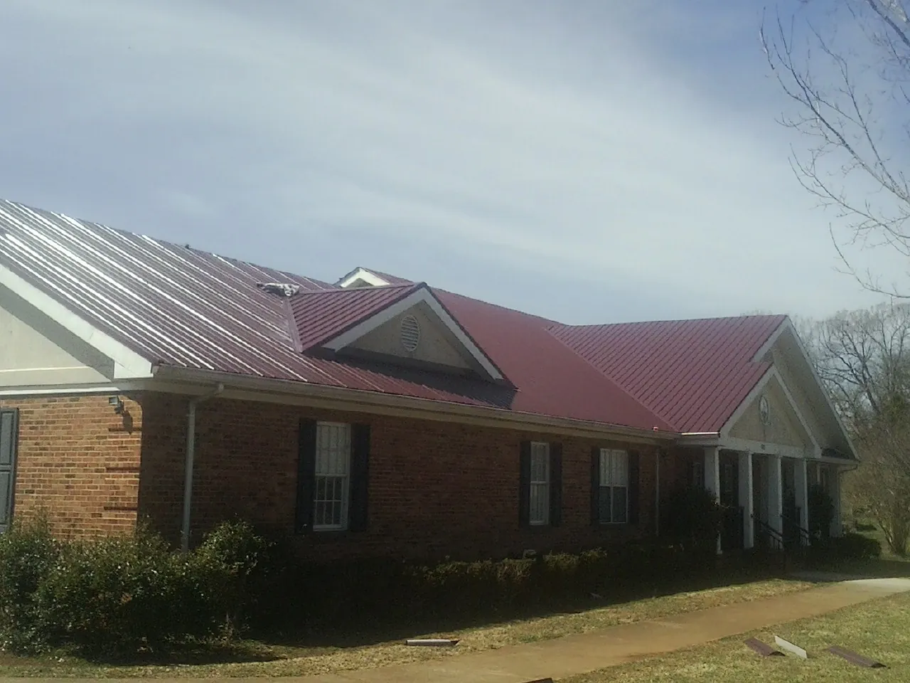 Red metal roof with gabled entries on a long brick building, from a Hail Damage Roof Repair job in Hope